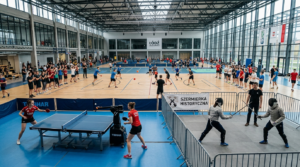 Akademicka Doba Sportu, Łódź, Polska. Sport studencki: gra w tenisa z robotem, dodgeball i szermierka historyczna studentów w nowoczesnej hali sportowej.
